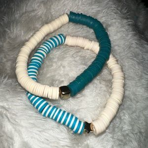 2 clay bracelets that are teal and light cream color with golden square and star